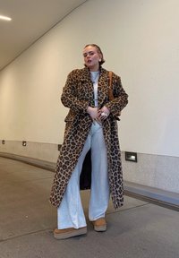 Μαύρο παλτό με λεοπάρ σχέδιο, κρέμα μπλούζα, γκρίζες παντελόνες σε φαρδιά γραμμή, καφέ μποτάκια. Τα αξεσουάρ περιλαμβάνουν πολλούς δακτυλίους και μια καφέ τσάντα ώμου. Εσωτερικός χώρος.