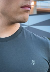 Γκρι βαμβακερό μπλουζάκι με στρογγυλή λαιμόκοψη, διακοσμημένο με μικρό λευκό λογότυπο "M O’P" στο αριστερό στήθος. Απλός και ομαλός σχεδιασμός και υφή.
