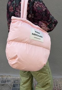 Oppblåst rosa handlenett med satengfinish og en hvit etikett med teksten "MADS NØRGAARD COPENHAGEN." Duftende yttertøy med blomstertrykk synlig.