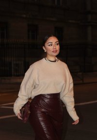 Beige oversized tröja i kombination med en hög midjad burgunderfärgad läderkjol. Anmärkningsbar pärlhalsband och liten burgunderfärgad handväska.