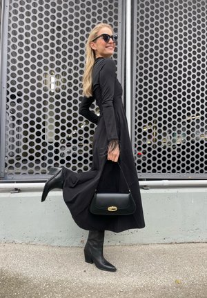 Vestido negro de manga larga con una silueta fluida y puños de plumas. Combinado con botas altas negras de tacón y un bolso negro estructurado.