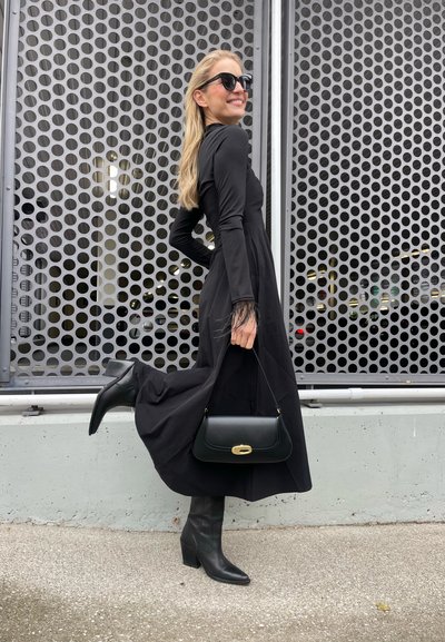 Vestido negro de manga larga con una silueta fluida y puños de plumas. Combinado con botas altas negras de tacón y un bolso negro estructurado.