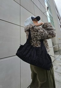 Mustmust tekstuuriga must käekott, millel on volditud disain, kantud halli, karvase äärmusega mantli peal. Väline sein sisaldab heledat värvi paneele.