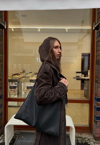 Čierna kožená taška tote s matným povrchom, priestranným trojuholníkovým tvarom, vystuženými rukoväťami a kvapkami vody na povrchu.