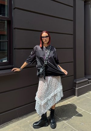 Overdreven zwart mesh shirt met sterdetail, gelaagde witte kanten rok met ruches, zwarte chunky vetersboots en schoudertas.