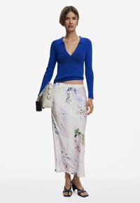 Blauwe geribde cropped cardigan met een kraag, gecombineerd met een bloemenpatroon, pastelroze rok. Accessoires omvatten een lichte tas en blauwe sandalen.