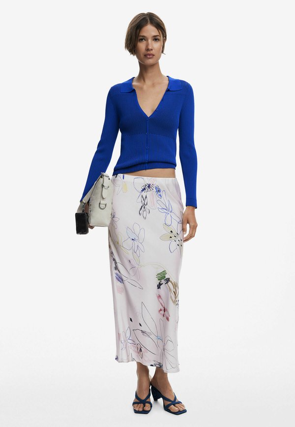 Cardigan cropped bleu à côtes avec col, associé à une jupe à motifs floraux de couleur rose pastel. Les accessoires comprennent un sac léger et des sandales bleues.
