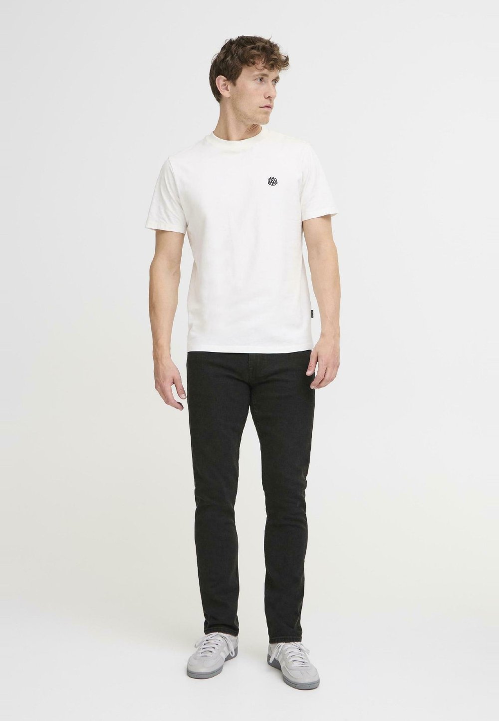 Valge puuvillane T-särk musta ümmarguse logoga rinna peal, koos mustade kitsaste teksade ja helesiniste tossudega.