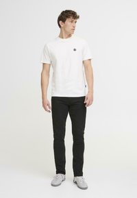 Valge puuvillane T-särk musta ümmarguse logoga rinna peal, koos mustade kitsaste teksade ja helesiniste tossudega.