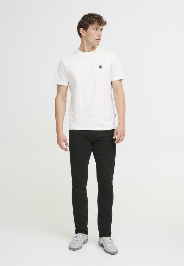 Valge puuvillane T-särk musta ümmarguse logoga rinna peal, koos mustade kitsaste teksade ja helesiniste tossudega.