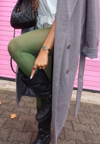 Γκρίζο παλτό σε σχέδιο ψαροκόκαλο πάνω από λευκή μπλ ούζα, με πράσινα κολάν και μαύρες μπότες μέχρι το γόνατο. Αξεσουάρ περιλαμβάνουν μια μαύρη τσάντα με καπιτονέ σχέδιο και ένα ρολόι.