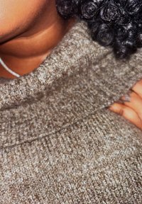 Maglione grigio lavorato a maglia con un colletto alto e ripiegato, caratterizzato da un tessuto testurizzato e da sottili variazioni di colore. Esibito su uno sfondo di tonalità della pelle.