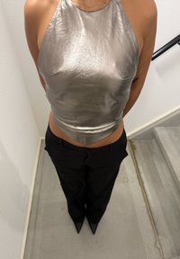 Personne portant un haut sans manches argenté métallique, un pantalon noir et des chaussures pointues noires, debout près d'un escalier en béton.