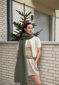 Cardigan leve e texturizado de creme com mangas curtas, emparelhado com uma blusa de malha bege, calções de creme e um lenço verde oversized.