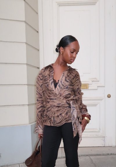 Blusa envolvente de estampado animal en tonos marrón y beige, con mangas largas y detalle de lazo en la cintura, combinada con pantalones negros y un bolso marrón.