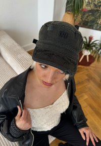 Căciulă neagră, uzată, cu un model decorativ, având un logo pe față. Materialul este țesătură cu un aspect casual și purtat.