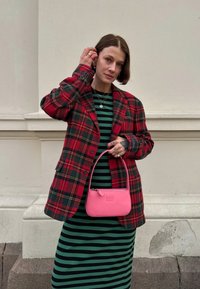 Red and green checked oversized blazer over a black and green striped dress; holding a small pink handbag with a zip closure.