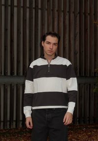 Mørkegrå og hvit stripete genser med kvartglidelås i halsen, med lange ermer og en avslappet passform, kombinert med svarte jeans.