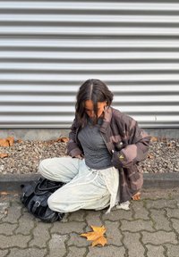 Hnedá maskáčová bunda, pruhované čierno-biele tričko, svetlo rifľové nohavice s čipkovaným lemom a čierna kabelka vedľa opadaného žltého listu.