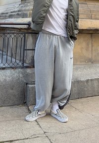 Grey jogging bottoms with an elasticated waistband and side stripes, paired with black and white checkered Vans trainers. Earth-toned bomber jacket worn on top.