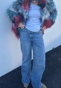 Daudzkrāsaina pūkaina kažokāda ar tirkīza, sarkaniem un baltiem toņiem, valkāta pār gaiši pelēku kreklu, kopā ar vaļīgām gaiši zilām džinsa biksēm un apaviem ar kniedēm.