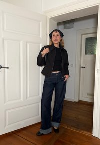 Czarna krótka kurtka na zamek, zestawiona z ciemnoniebieskimi spodniami typu wide-leg z podwiniętym dołem. Uzupełniona czarną chustą bandaną i butami.