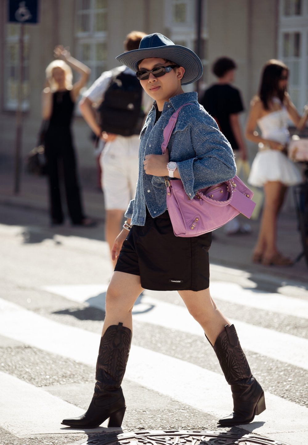 Τζιν πουκάμισο, μαύρες σορτς, μαύρες καουμπόικες μπότες και μωβ τσάντα. Αξεσουάρ περιλαμβάνουν γυαλιά ηλίου και ρολόι χειρός. Σκηνικό δρόμου.