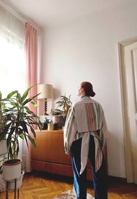 Triibuline särk rohelises, roosas ja sinises värvitoonis, millel on seljal lipsukujundus; kombineeritud tumedate denimist teksadega, taustal taimed ja puidust mööbel.