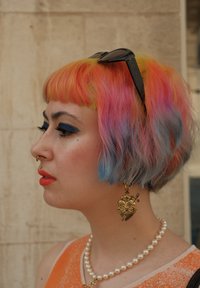 Kleurvol, gelaagd haar met roze, gele en blauwe tinten. Kenmerkt gouden hartvormige oorbellen, een zonnebril en een parelketting.