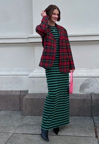 A red and black check blazer worn over a green and black striped dress, teamed with heeled black boots and a small pink handbag.