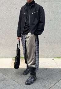 Μαύρο μπουφάν με φερμουάρ πάνω από μαύρη πουκαμίσα, γκρι σατέν παντελόνι με καρ�ό πλαϊνές ρίγες, μαύρες δερμάτινες μπότες και μαύρη τσάντα ώμου.