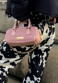 Sac à main rose matelassé avec quincaillerie dorée et chaîne, présentant des détails de surface texturée. Associé à un pantalon à motifs noir et blanc.