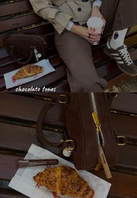 Hnědá semišová kabelka se zlatými kovovými doplňky, croissant na bílém papíře a hnědý rtěnkový produkt na dřevěné lavičce, kde jsou vidět ponožky a boty.