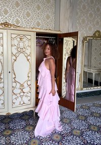Vestido de tono rosa claro, con volantes y diseño de cuello halter. El fondo presenta un armario ornamentado y azulejos en el suelo con patrones. El espejo refleja la imagen.
