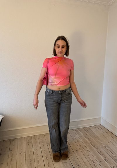 Camiseta corta rosa con un gráfico de palmera, combinada con jeans rectos de un tono azul claro y zuecos forrados de piel en marrón.