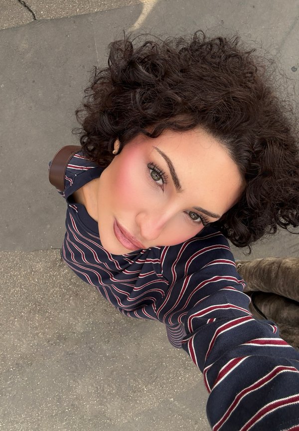 Le mannequin porte une chemise à rayures bleu marine à manches longues avec des lignes maroon et blanches ; cheveux bouclés ; perspective en gros plan ; le sol est visible en dessous.