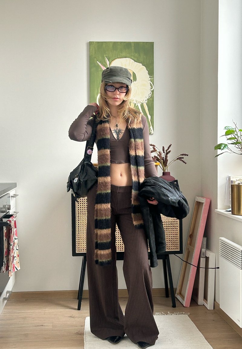 Completo coordinato marrone a costine con pantaloni ampi, abbinato a una sciarpa a righe e una giacca di pelle. Completa il look un berretto grigio e occhiali rotondi.