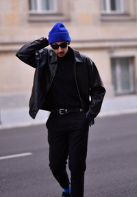 Μαύρο δερμάτινο μπουφάν πάνω από μαύρο τζινού, μαύρο παντελόνι, μπλε σκουφάκι και σκούρα γυαλιά ηλίου με μια λαμπερή ζώνη και μπλε κάλτσες.