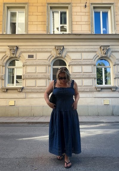 Vestido largo fluido de color azul oscuro con un corpiño fruncido, con encaje en el dobladillo y tirantes anchos; combinado con un bolso negro y chanclas.