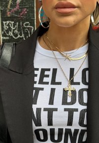 Blazer negru peste o cămașă albă cu dungi, având un text îndrăzneț în negru. Lănțișoare de aur suprapuse, inclusiv cu modele de cruce și stea. Cercei mari din argint în formă de cerc.