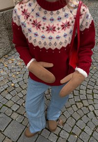 Rode gebreide trui met een crème Fair Isle-patroon, blauwe en roze accenten; bruine suède wanten; lichtblauwe uitlopende jeans; bruin schoeisel.