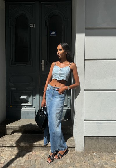 Top corto de mezclilla azul claro con detalle de cordones, combinado con una larga falda de mezclilla azul claro. Bolso negro y sandalias planas con hebillas.