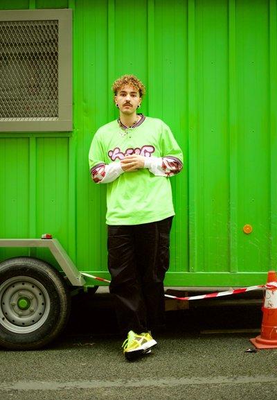 Jersey holgado de color verde neón con un estampado gráfico, combinado con pantalones cargo negros. Zapatillas brillantes con acentos reflectantes y cabello rizado.