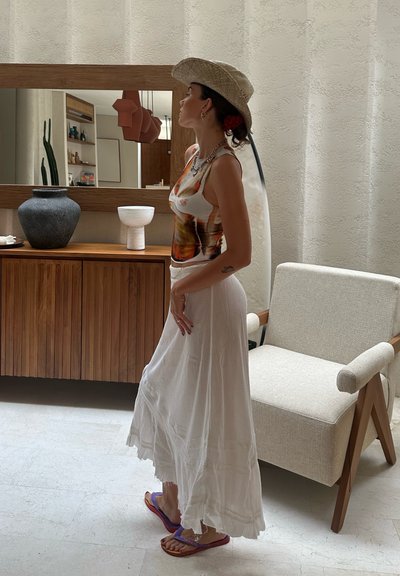 Falda maxi blanca y fluida con un dobladillo con volantes y una camiseta sin mangas de colores ajustada. Un notable sombrero de paja y sandalias moradas realzan el conjunto.