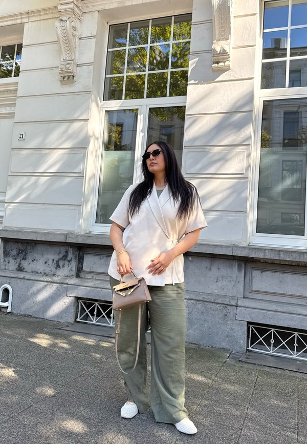 Beige bőrdzseki, oliva zöld széles lábú nadrág, fehér texturált slip-on cipők és egy kicsi barna válltáska.