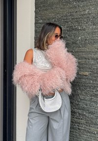 Pink fluffy outerwear, sequinned sleeveless top, grey wide-legged trousers, and a small silver handbag against a stone wall.