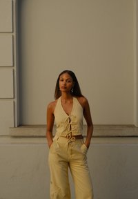 Gelbes Leinen-Haltertop mit Frontbindebändern, kombiniert mit passenden, hochgeschnittenen, lockeren Hosen mit Seitentaschen und Auschnitte. Einfacher, strukturierter Stoff.