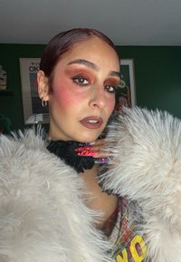 Model draagt een pluizige witte imitatieleren jas, kleurrijke oversized nagels, en een zwarte gerimpelde kraag; ogen benadrukt met warme oranje tinten.