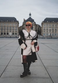 Hvit kjole med svarte detaljer, kombinert med en svart og hvit pelsjakke. Tilbehør inkluderer solbriller og en rosa veske. Skinnende svarte platåstøvler.