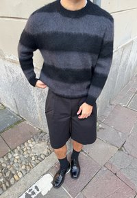 Maglione a righe nere e grigie realizzato in materiale soffice, abbinato a pantaloncini neri e scarpe nere lucide. Superficie strutturata con polsini a coste.